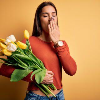 Gähnende Frau mit Frühjahrsblumen in der Hand als Symbol für Frühjahrsmüdigkeit